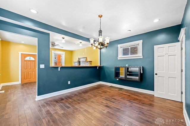 interior space featuring pendant lighting, kitchen peninsula, ceiling fan with notable chandelier, and dark hardwood / wood-style floors