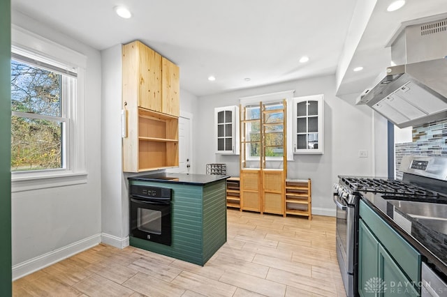 kitchen with island exhaust hood, black oven, light wood-type flooring, green cabinetry, and stainless steel range with gas cooktop