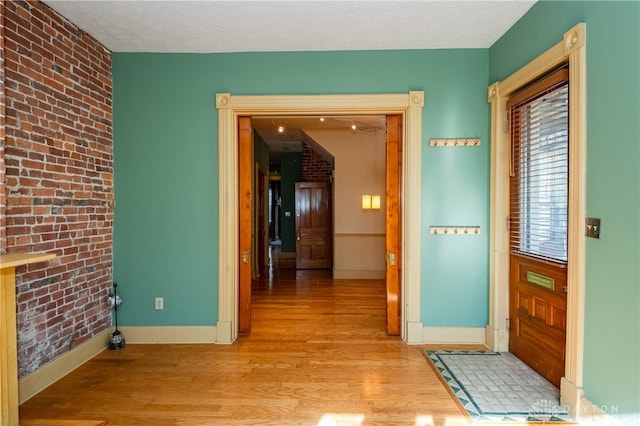 hallway with brick wall, a textured ceiling, and light hardwood / wood-style flooring