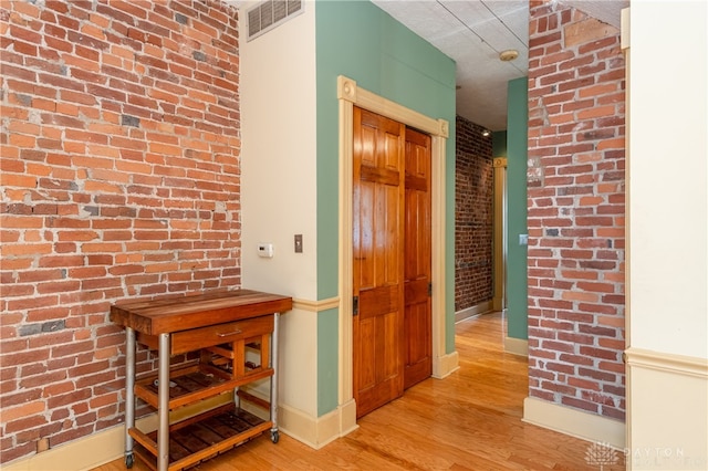 corridor with brick wall and light hardwood / wood-style flooring