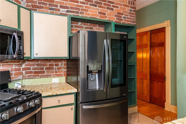 kitchen with light wood-type flooring, appliances with stainless steel finishes, brick wall, and light stone countertops