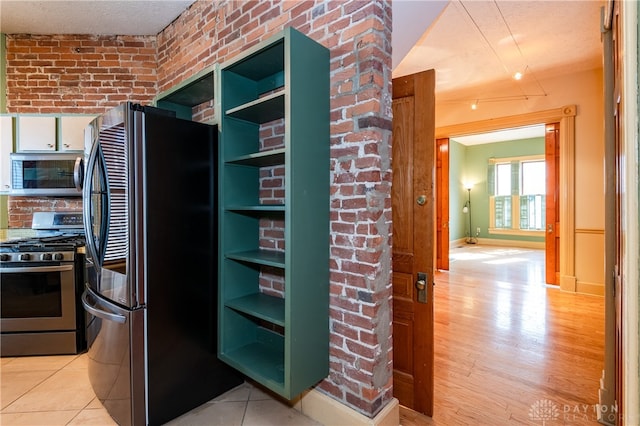 kitchen with light wood-type flooring, stainless steel appliances, brick wall, and a textured ceiling