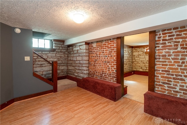 basement with brick wall, wood-type flooring, and a textured ceiling