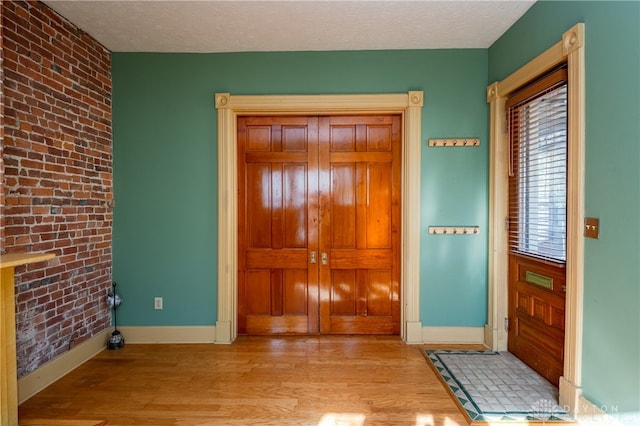 entryway featuring light hardwood / wood-style floors, a textured ceiling, and brick wall