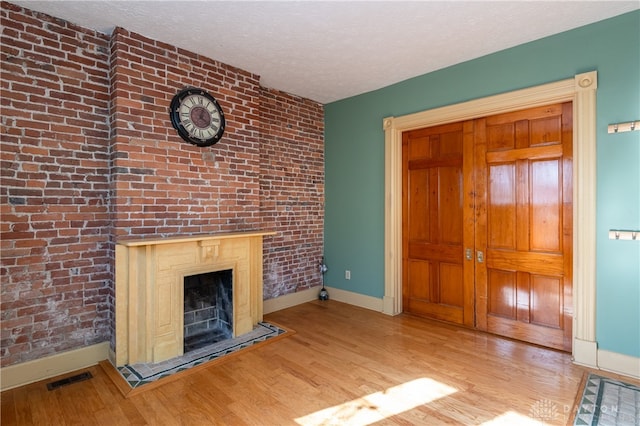 unfurnished living room with light hardwood / wood-style floors, brick wall, and a textured ceiling