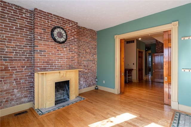 unfurnished living room featuring a textured ceiling, light hardwood / wood-style floors, and brick wall