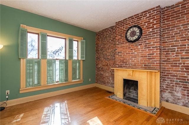 unfurnished living room with light wood-type flooring, a fireplace, brick wall, and a textured ceiling