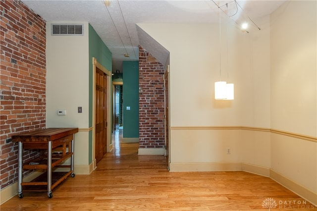 spare room with wood-type flooring, a textured ceiling, and brick wall