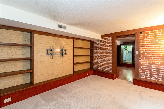 carpeted spare room featuring brick wall and a textured ceiling