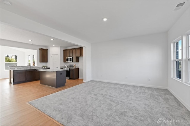 kitchen featuring visible vents, open floor plan, a center island, appliances with stainless steel finishes, and dark brown cabinets