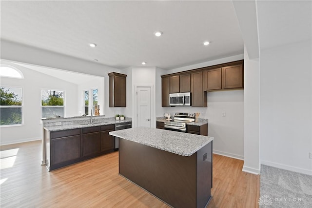 kitchen with dark brown cabinets, light stone countertops, light wood-style floors, and appliances with stainless steel finishes