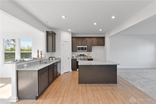 kitchen with recessed lighting, a sink, stainless steel appliances, dark brown cabinetry, and a center island