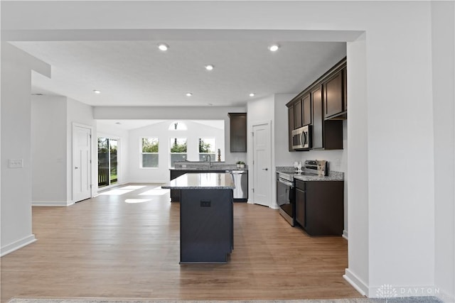 kitchen featuring stainless steel appliances, a kitchen island, dark brown cabinetry, and light wood-style flooring