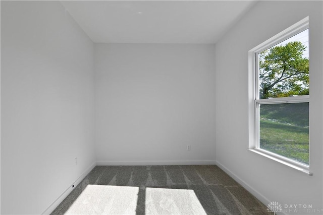 empty room with plenty of natural light, baseboards, and dark colored carpet