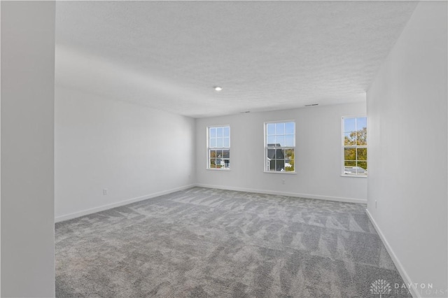 empty room with a textured ceiling, baseboards, and carpet floors