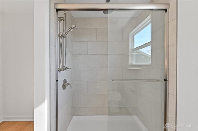 full bath with wood finished floors, baseboards, and a stall shower