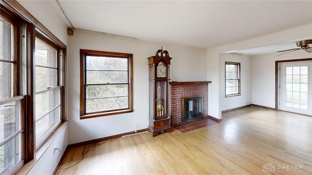 unfurnished living room featuring a brick fireplace, light wood-type flooring, plenty of natural light, and ceiling fan