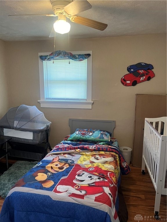 bedroom with a textured ceiling, ceiling fan, and dark hardwood / wood-style floors