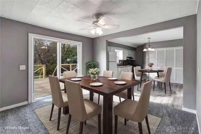 carpeted dining space featuring ceiling fan with notable chandelier