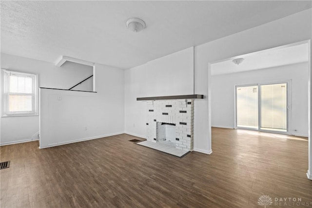 unfurnished living room with dark hardwood / wood-style flooring, a textured ceiling, and a brick fireplace