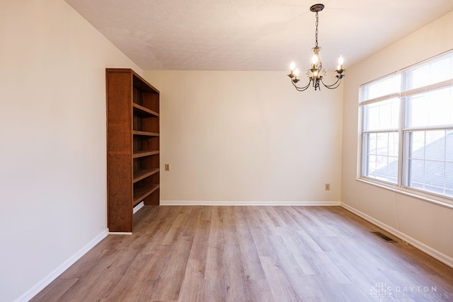 unfurnished room with light wood-type flooring, an inviting chandelier, and a textured ceiling