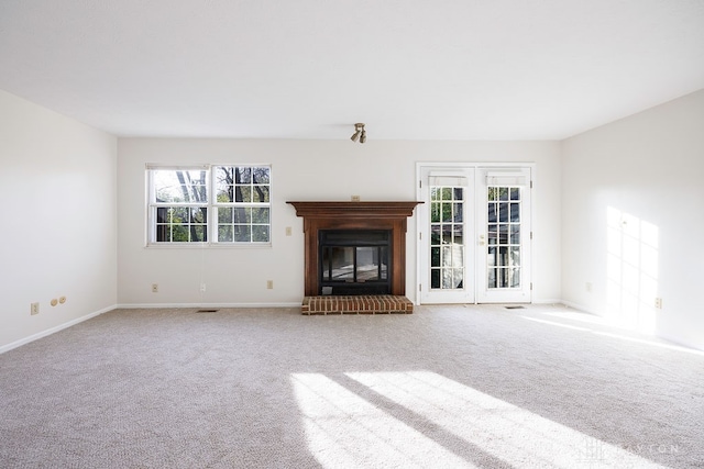 unfurnished living room featuring a brick fireplace, french doors, and light colored carpet