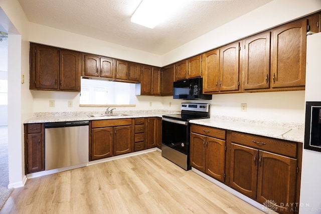 kitchen with light stone counters, a textured ceiling, sink, light wood-type flooring, and appliances with stainless steel finishes