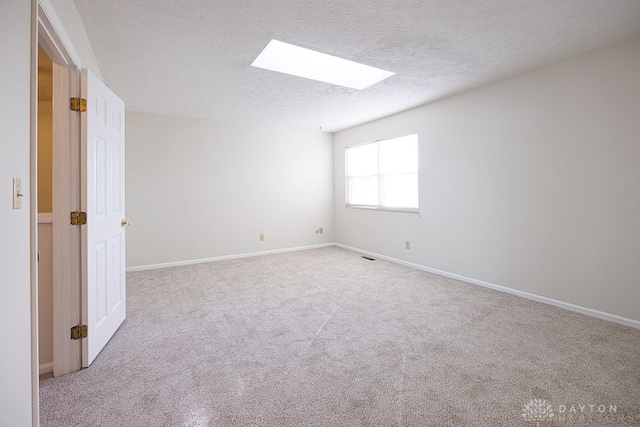 empty room with a skylight, a textured ceiling, and light colored carpet