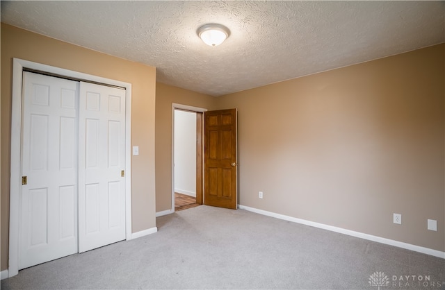 unfurnished bedroom with light carpet, a closet, and a textured ceiling