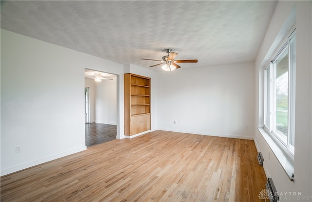 spare room featuring built in shelves, light hardwood / wood-style floors, a textured ceiling, and ceiling fan