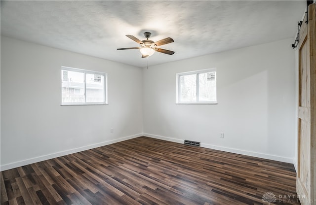 unfurnished room with dark hardwood / wood-style floors, a barn door, a healthy amount of sunlight, and ceiling fan