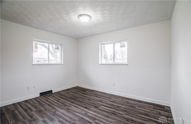 empty room featuring plenty of natural light, dark hardwood / wood-style floors, and a textured ceiling