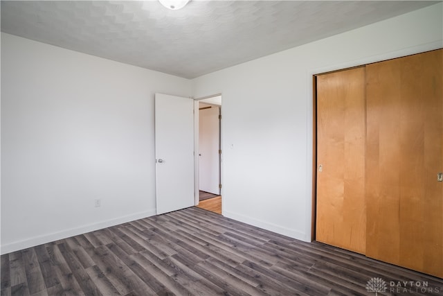 unfurnished bedroom with a textured ceiling, dark hardwood / wood-style floors, and a closet