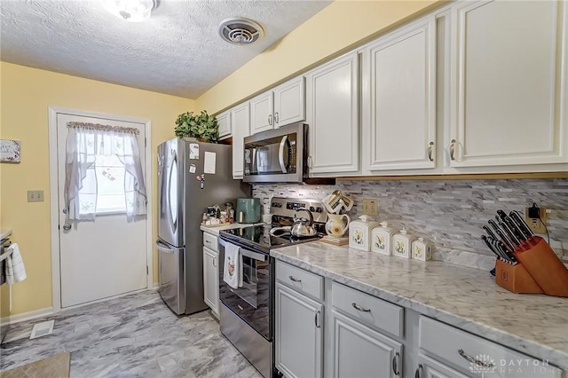 kitchen with light stone countertops, decorative backsplash, stainless steel appliances, and a textured ceiling