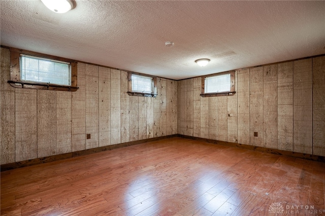 basement featuring wooden walls, a textured ceiling, and hardwood / wood-style flooring