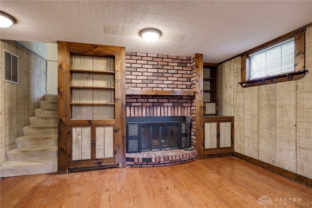 unfurnished living room with hardwood / wood-style floors, wood walls, a textured ceiling, and a brick fireplace