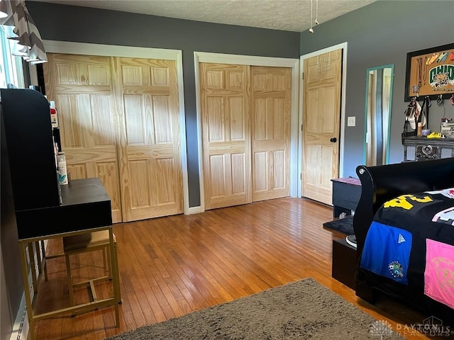 bedroom featuring multiple closets, wood-type flooring, and a textured ceiling