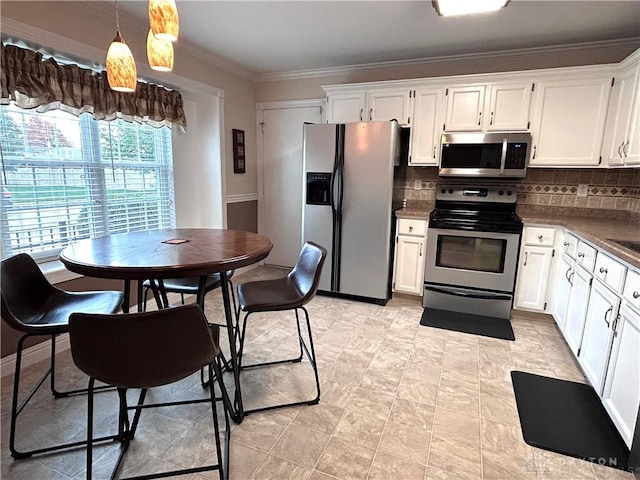 kitchen with hanging light fixtures, ornamental molding, tasteful backsplash, white cabinetry, and stainless steel appliances