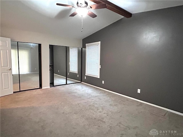 unfurnished bedroom with lofted ceiling with beams, ceiling fan, light carpet, and two closets