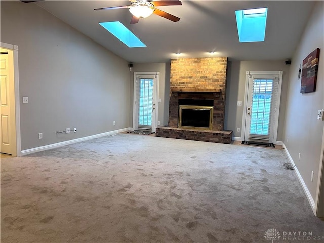 unfurnished living room featuring vaulted ceiling with skylight, carpet floors, a wealth of natural light, and a brick fireplace