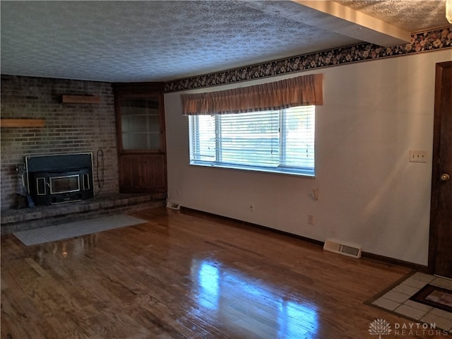 unfurnished living room with hardwood / wood-style floors, beamed ceiling, a wood stove, and a textured ceiling