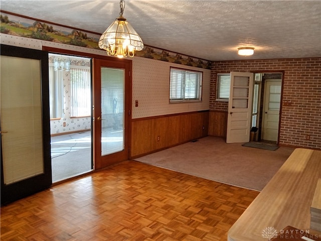 unfurnished dining area with wood walls, light parquet flooring, and a textured ceiling