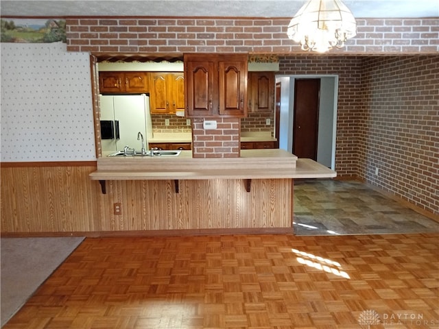 kitchen with light parquet floors, white fridge with ice dispenser, sink, and a breakfast bar area