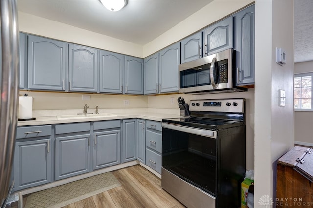 kitchen with appliances with stainless steel finishes, a textured ceiling, light hardwood / wood-style floors, and sink