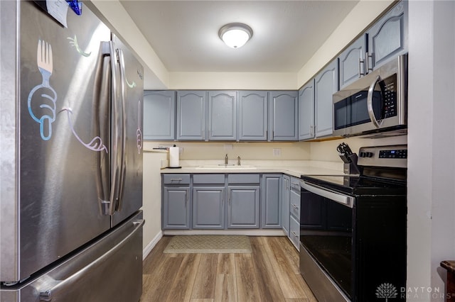 kitchen featuring appliances with stainless steel finishes, hardwood / wood-style flooring, gray cabinetry, and sink