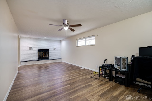 living room with hardwood / wood-style floors, a brick fireplace, ceiling fan, a textured ceiling, and brick wall