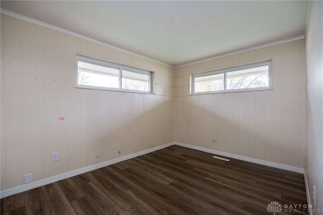 empty room featuring crown molding, a wealth of natural light, dark wood-type flooring, and wood walls