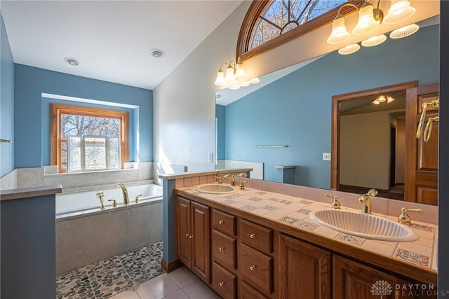 bathroom featuring vanity, tile patterned flooring, vaulted ceiling, and tiled tub