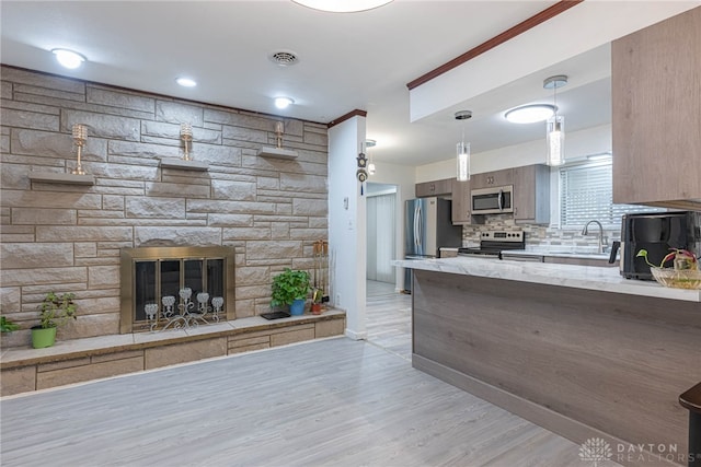 kitchen featuring tasteful backsplash, stainless steel appliances, hanging light fixtures, sink, and light hardwood / wood-style floors