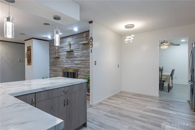 kitchen with a stone fireplace, pendant lighting, light stone countertops, ceiling fan, and light hardwood / wood-style flooring